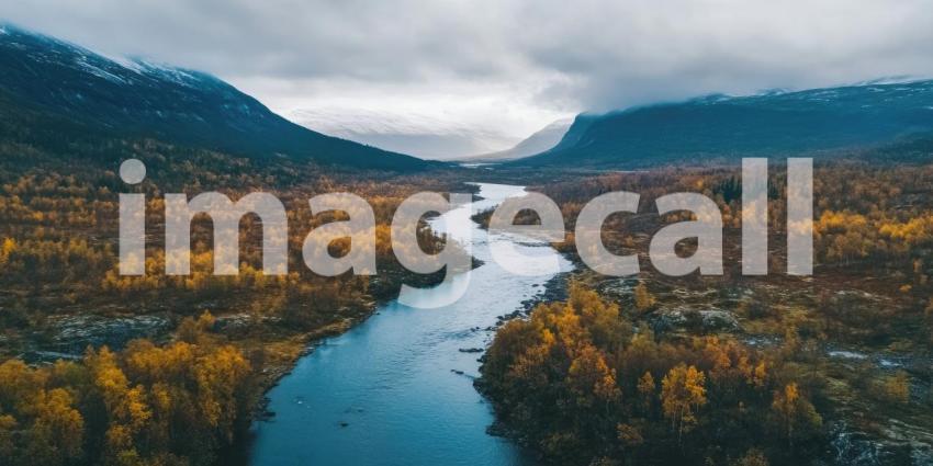 Aerial View of a Serpentine River Flowing Through a Valley of Autumnal Trees, with Snow-capped Mountains in the Distance